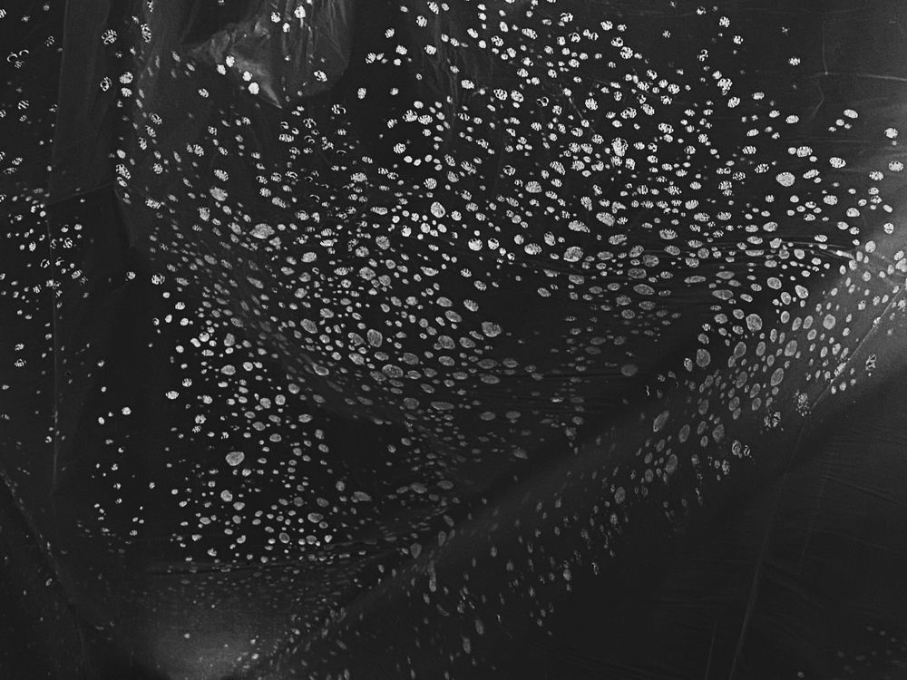 A black and white image of water droplets on a clear plastic bag, looking a bit like stars.
