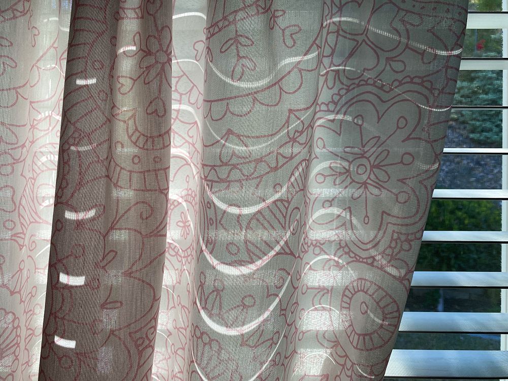 Wavy lines of light showing through a patterned curtain in front of a window with Venetian blinds