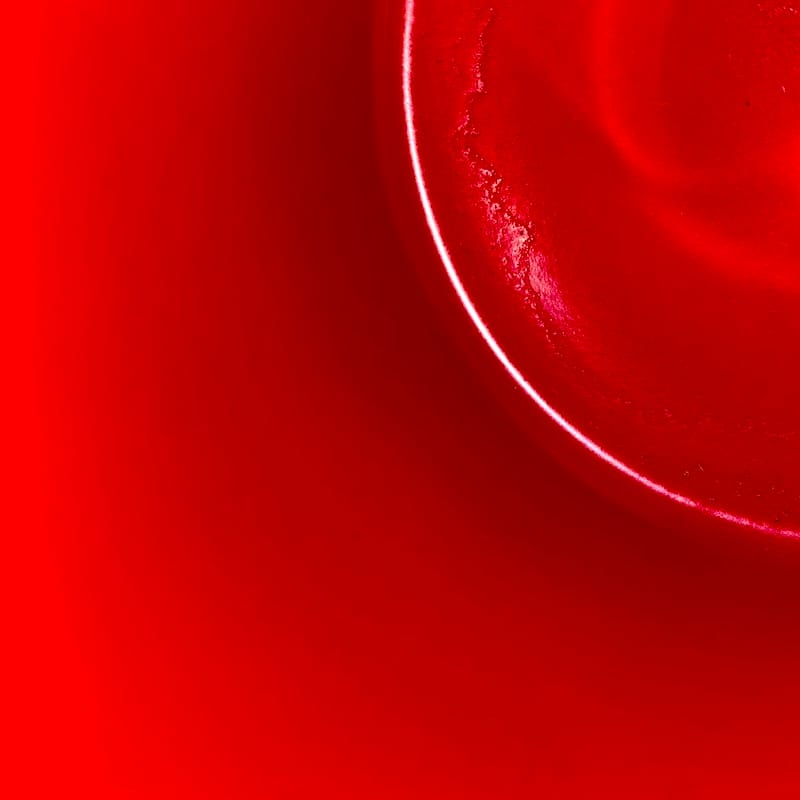 An abstract image of the inside of a red mug. The image is square and bright red, with the curve of the bottom of the cup making a quarter circle that cuts the top-right of the image. Tea residue is visible at the bottom of the cup.